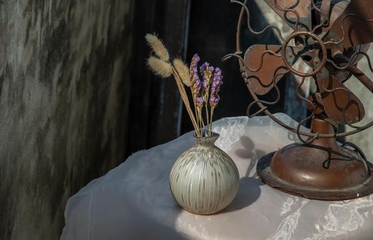 Dried flowers in Ceramic vase on pink textured table cloth and vintage fan with Old cement wall. Home decor, Selective focus.