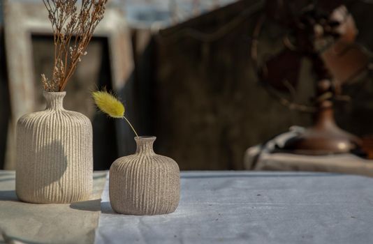 Dried flowers in Two small ceramic vase on white textured table cloth and vintage fan with Old cement wall at the balcony house. Home decor, Selective focus.