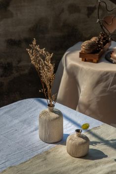 Dried flowers in Two small ceramic vase on white textured table cloth with Old cement wall. Home decor, Selective focus.