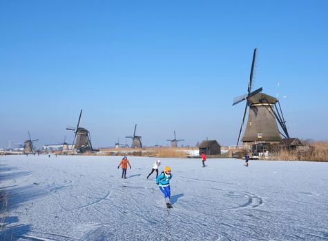 kinderdijk, netherlands, 12 february 2021: people skate on the ice near kinderdijk with al lot of windmills in holland on sunny winter day