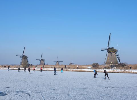 kinderdijk, netherlands, 12 february 2021: people skate on the ice near kinderdijk with al lot of windmills in holland on sunny winter day