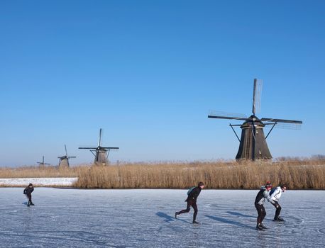 kinderdijk, netherlands, 12 february 2021: people skate on the ice near kinderdijk with al lot of windmills in holland on sunny winter day
