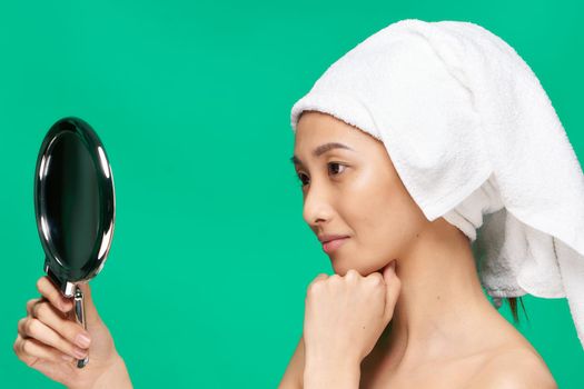 woman of Asian appearance with a towel on her head naked shoulders Looking in the mirror. High quality photo