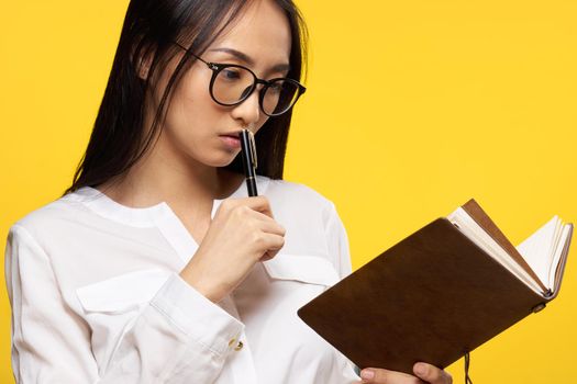 pretty brunette with glasses holding a notebook in the hands of students learning yellow background. High quality photo