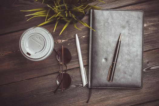 book with black cover and lies on a wooden table and a pen pencil jobs glasses flower potted coffee cup. High quality photo