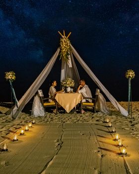 couple men and woman having romantic dinner with candle lights on the beach in Thailand, European men and Asian woman dinner on the beach Valentine concept. Romantic dinner on the beach