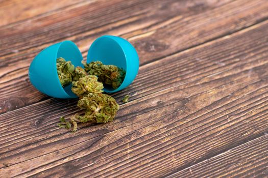A Blue Plastic Easter Egg With Light Green Cannabis Nugs Coming Out of It on a Wooden Table