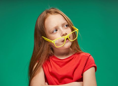 cheerful red-haired girl yellow glasses emotions green background childhood. High quality photo
