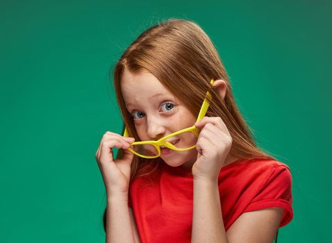 cheerful red-haired girl yellow glasses emotions green background childhood. High quality photo