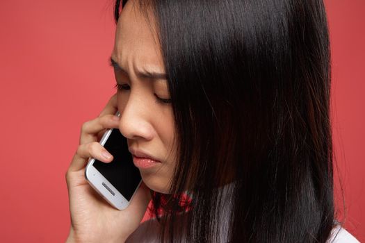 sad asian woman talking on the phone close-up red background. High quality photo