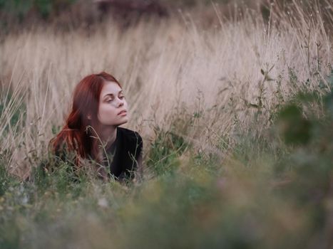 red-haired woman in a black dress lies in a field on dry grass in nature. High quality photo