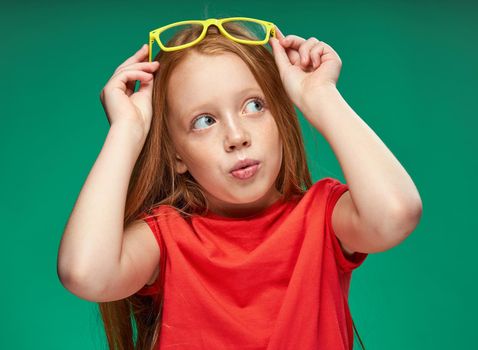 cute red-haired girl with glasses gesturing with her hands school childhood green background. High quality photo