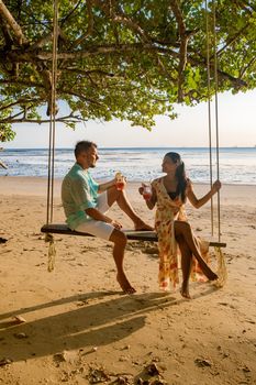 Happy traveler couple relaxing on the swing and looking beautiful nature, Andaman sea, Krabi, Tourist sea beach Thailand, Asia, Summer holiday vacation travel trip. European man and an Asian woman