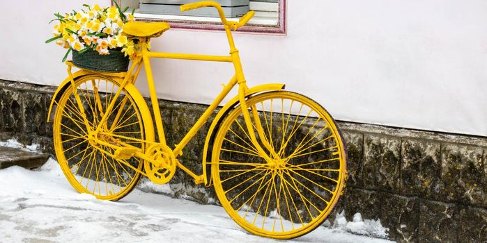An old yellow bicycle stands against a wall in winter, in vintage style.