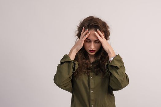 A beautiful girl has a migraine and a headache. A young woman holds her hands to her temples and massages them. On a gray background. copy space