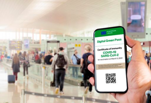 The digital green pass of the european union with the QR code on the screen of a mobile held by a hand with blurred airport in the background. Immunity from Covid-19. Travel without restrictions.