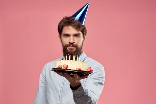 Man with cake in a plate and in a blue shirt on a pink background birthday holidays cropped view. High quality photo