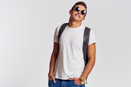 man in sunglasses with a backpack on his back and in a white t-shirt on a light background cropped view of emotion. High quality photo