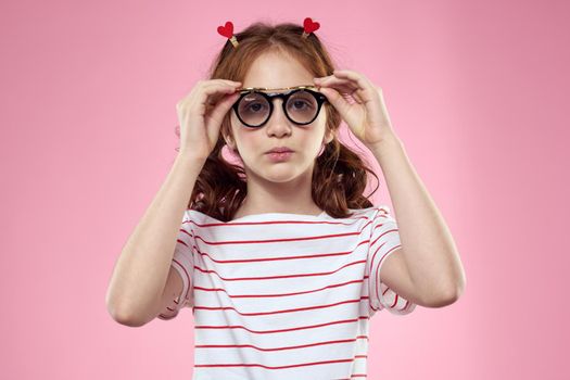 little girl in fashionable glasses and clothespins on her hair emotions pink background hearts. High quality photo
