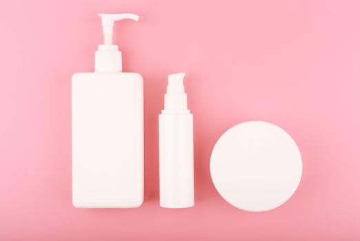 Body cream, face cream and scrub in white tubes on pink background. Flat lay with set of cosmetic products for skin care and beauty treatment at home