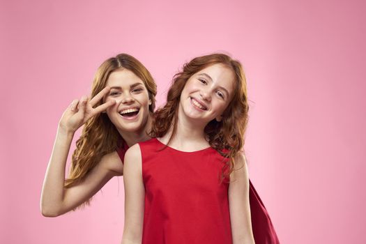 Cheerful mom and daughter wearing red dresses are standing next to joy family on pink background. High quality photo