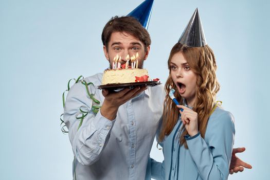 man and woman celebrate birthday with cake and in hats on blue background. High quality photo
