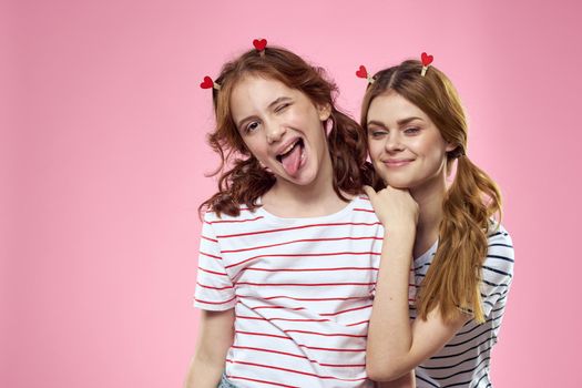 Happy sisters are having fun on a pink background and heart-shaped clothespins on their heads. High quality photo