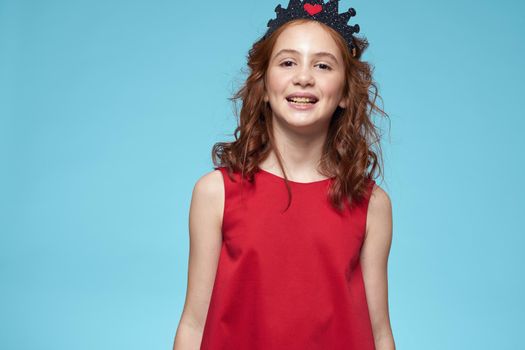 Girl with curly hair with a crown on her head red dress lifestyle blue background. High quality photo