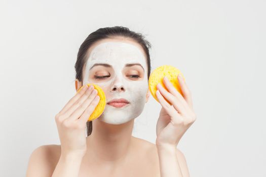 joyful woman with bare shoulders cream mask on face scrub sponges in hands. High quality photo