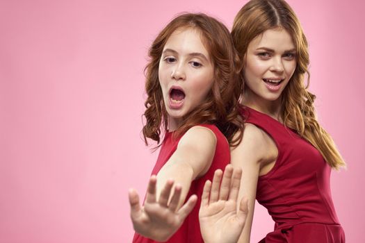 Mom and daughter in red dresses hugs fun grimace childhood joy pink background. High quality photo