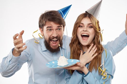 energetic man and woman with a cake and in hats celebrate a birthday on a light background. High quality photo