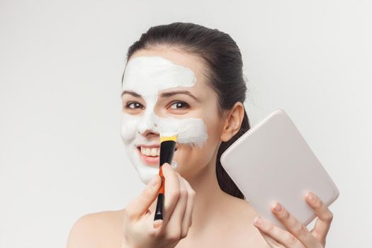 brunette naked shoulders applying cream brush on face. High quality photo