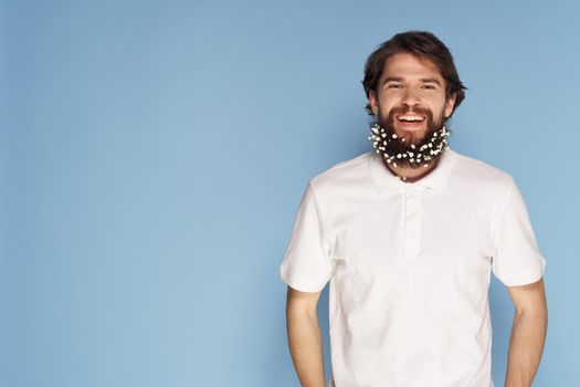 Bearded man with flowers in his hair ornaments fun white t-shirt blue background. High quality photo