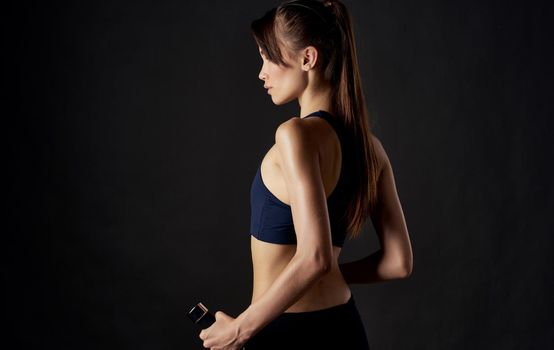 sportswoman with dumbbells in her hands on a black background slim figure short top. High quality photo