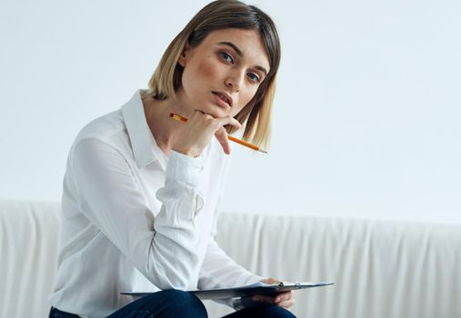 A woman sits on a sofa In a bright room in a shirt and papers on her lap. High quality photo