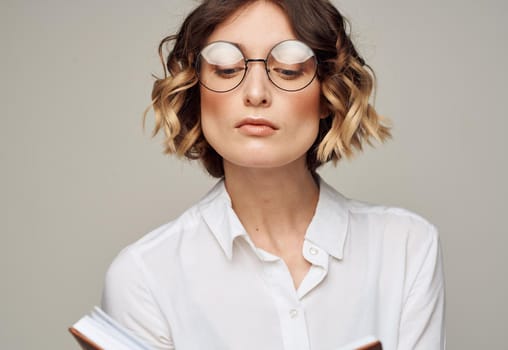 Woman with a notepad in her hands and wearing glasses on a gray background cropped view of a Light shirt. High quality photo