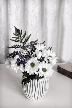 On the table in a white ceramic vase is a bouquet of beautiful white chrysanthemums. Front view, copy space