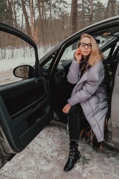 Attractive young female looks out the car window waiting for a trip and smile. Winter travel. Woman sitting in the car. Concept for car rental