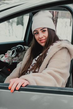 Attractive young female looks out the car window waiting for a trip and smile. Winter travel. Woman sitting in the car. Concept for car rental