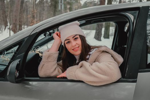 Attractive young female looks out the car window waiting for a trip and smile. Winter travel. Woman sitting in the car. Concept for car rental