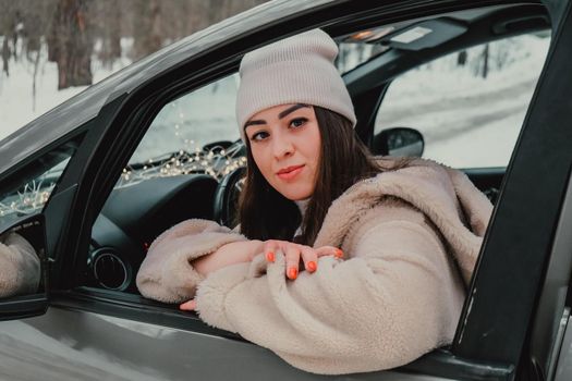 Attractive young female looks out the car window waiting for a trip and smile. Winter travel. Woman sitting in the car. Concept for car rental