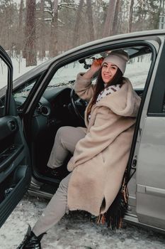 Attractive young female looks out the car window waiting for a trip and smile. Winter travel. Woman sitting in the car. Concept for car rental