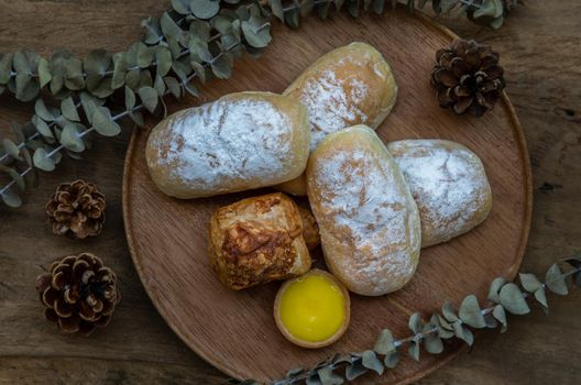 Homemade sweet cream soft buns, Baked croissant sausage and Lemon tart with Dried flowers on round wooden plate over rustic wooden table. Bakery and dessert concept, Selective focus.