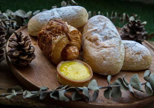 Homemade sweet cream soft buns, Baked croissant sausage and Lemon tart with Dried flowers on round wooden plate over rustic wooden table. Bakery and dessert concept, Selective focus.