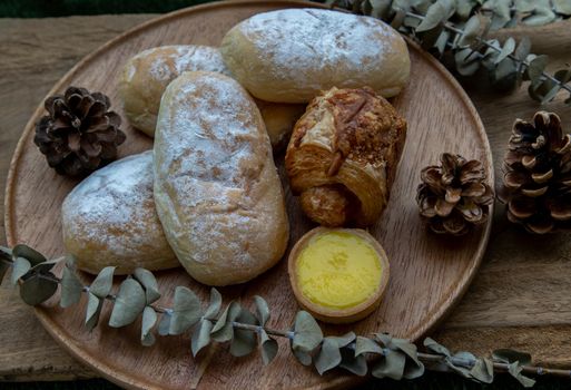 Homemade sweet cream soft buns, Baked croissant sausage and Lemon tart with Dried flowers on round wooden plate over rustic wooden table. Bakery and dessert concept, Selective focus.