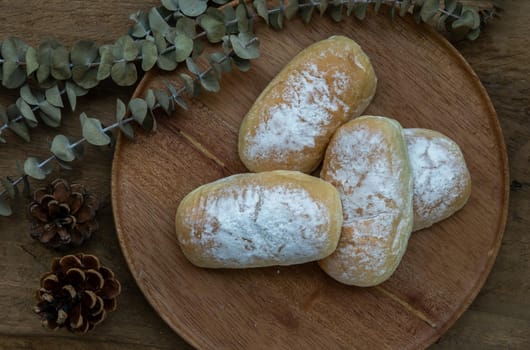Four homemade sweet cream soft buns and sprinkled with icing sugar on round wooden plate over rustic wooden table. Bakery and dessert concept, Selective focus.