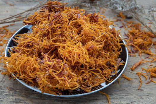 Thai sweets made from shredded sweet potato coated with sugar (Thai sweetmeat made of fried sweet potato) on ceramic plate over rustic wooden background. Selective focus