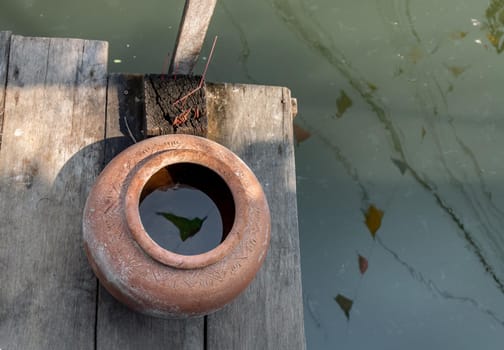 Old big earthen jar or Vintage clay jar for water storage on pier waterfront balcony pavilion at thai ancient style house.  Selective focus.