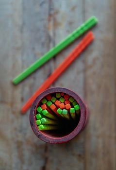 Orange and Green plastic chopsticks grouped in a wooden holder placed on old wooden table in noodle shop. For customers to use. Selective focus.