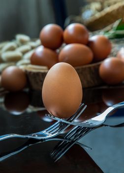 Fresh chicken egg (Hen egg) balanced on a composition of two intertwined forks with fresh chicken eggs on wood background. Selective focus.